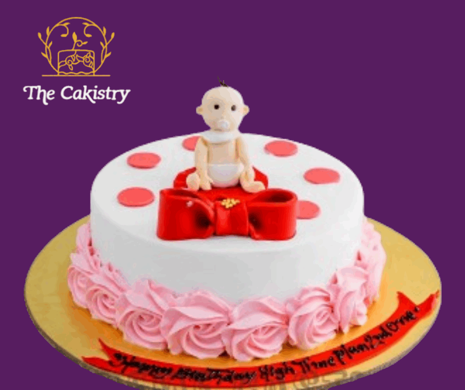 Baby-themed cake with pink decorations and a baby figurine on a purple background, featuring 'The Cakistry' logo.