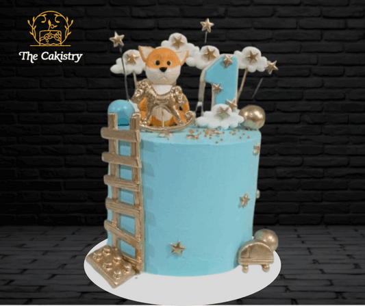 Decorative cake with a teddy bear figure on a blue background, featuring 'The Cakistry' branding.