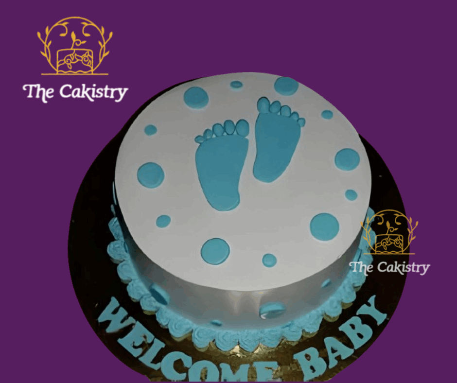 Baby shower cake with blue footprints and 'Welcome Baby' text on a purple background, branded with 'The Cakistry'.