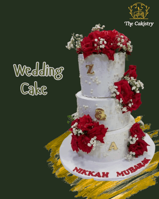 Three-tiered wedding cake decorated with red flowers and gold letters, featuring 'The Cakistry' logo.